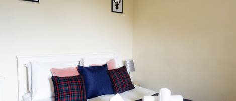 A neatly made bed with plaid bedding, a lamp, and two framed deer heads on the wall.