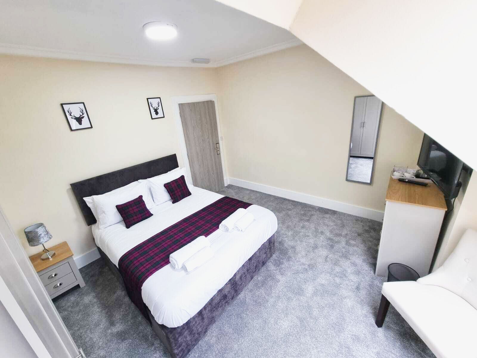 A neatly arranged hotel room with a bed, a bedside table, a chair, and a desk with a television.