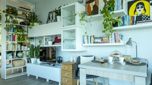 A well-organized room with multiple white shelves filled with books, decorative items, and plants. There is a dining table with chairs, a lamp, and a small coffee table. - Villa Mayas - Scopello with private pool (Castellammare del Golfo)