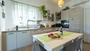 A modern kitchen with a central island, built-in appliances, and a dining area with chairs. - Villa Mayas - Scopello with private pool (Castellammare del Golfo)