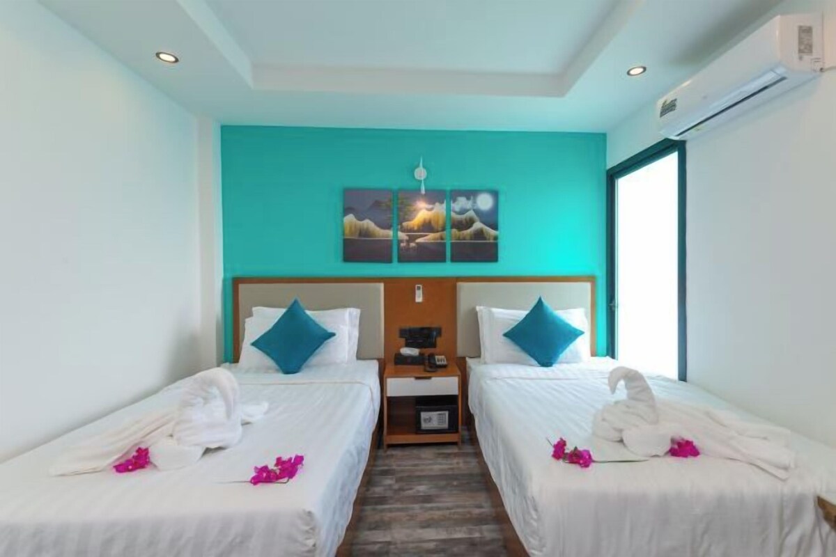 Una habitación de hotel con dos camas individuales, una mesita de noche, una obra de arte en la pared y una ventana.