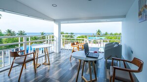 A spacious balcony with a view of the ocean, furnished with wooden chairs and a table, and a laptop on the table. - Funplace Beach (Himmafushi)