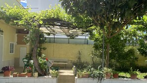 Uma área de varanda coberta com um banco, plantas em vasos e uma pequena entrada.
