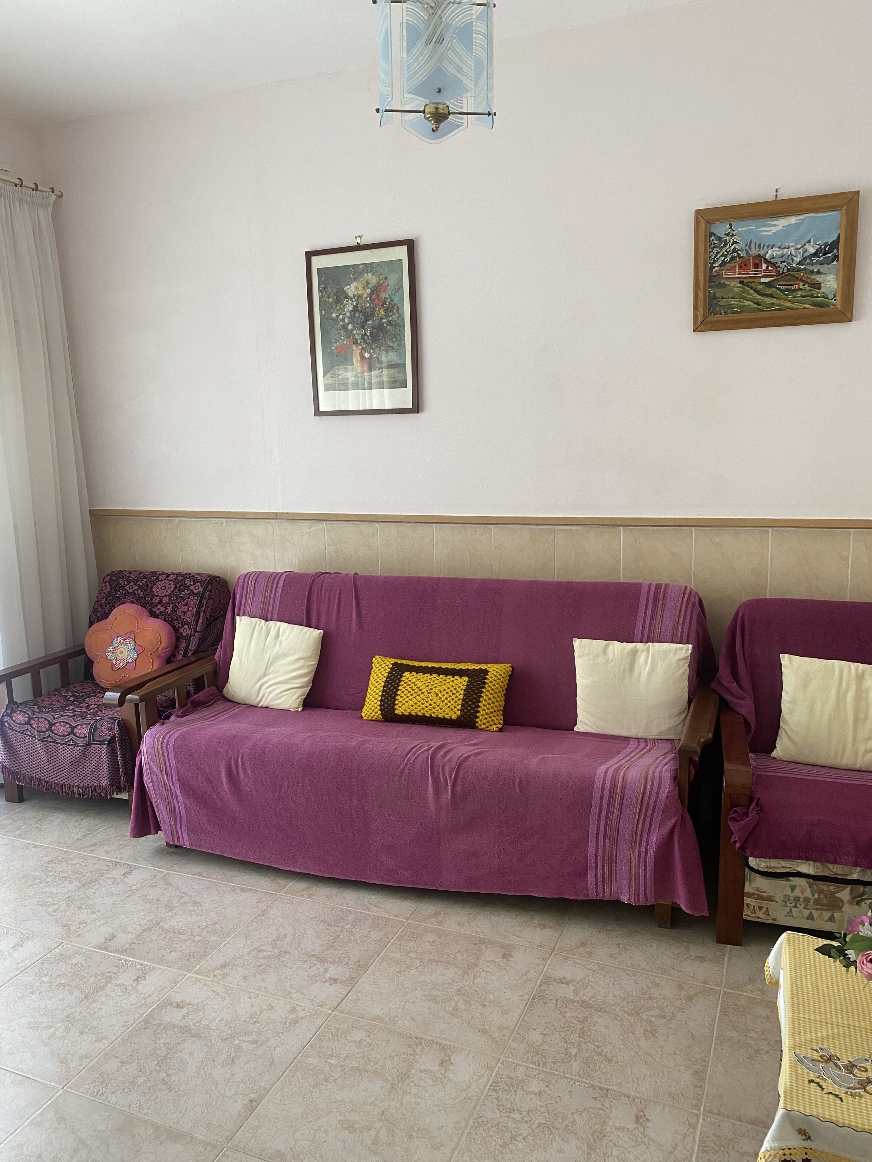 A living room with a purple sofa, a wooden chair, and a small table with a yellow tablecloth.