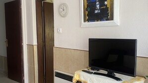 Uma sala de estar com uma televisão em um suporte, um relógio na parede e um quadro acima da TV.