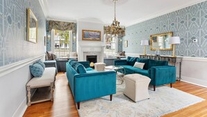 A spacious living room with teal sofas, a fireplace, and patterned wallpaper. - The Jasmine Suite | Revisit History (Charleston)