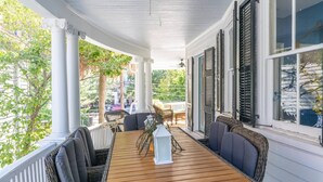 A covered porch with a wooden table and chairs, white columns, and shutters. - The Jasmine Suite | Revisit History (Charleston)