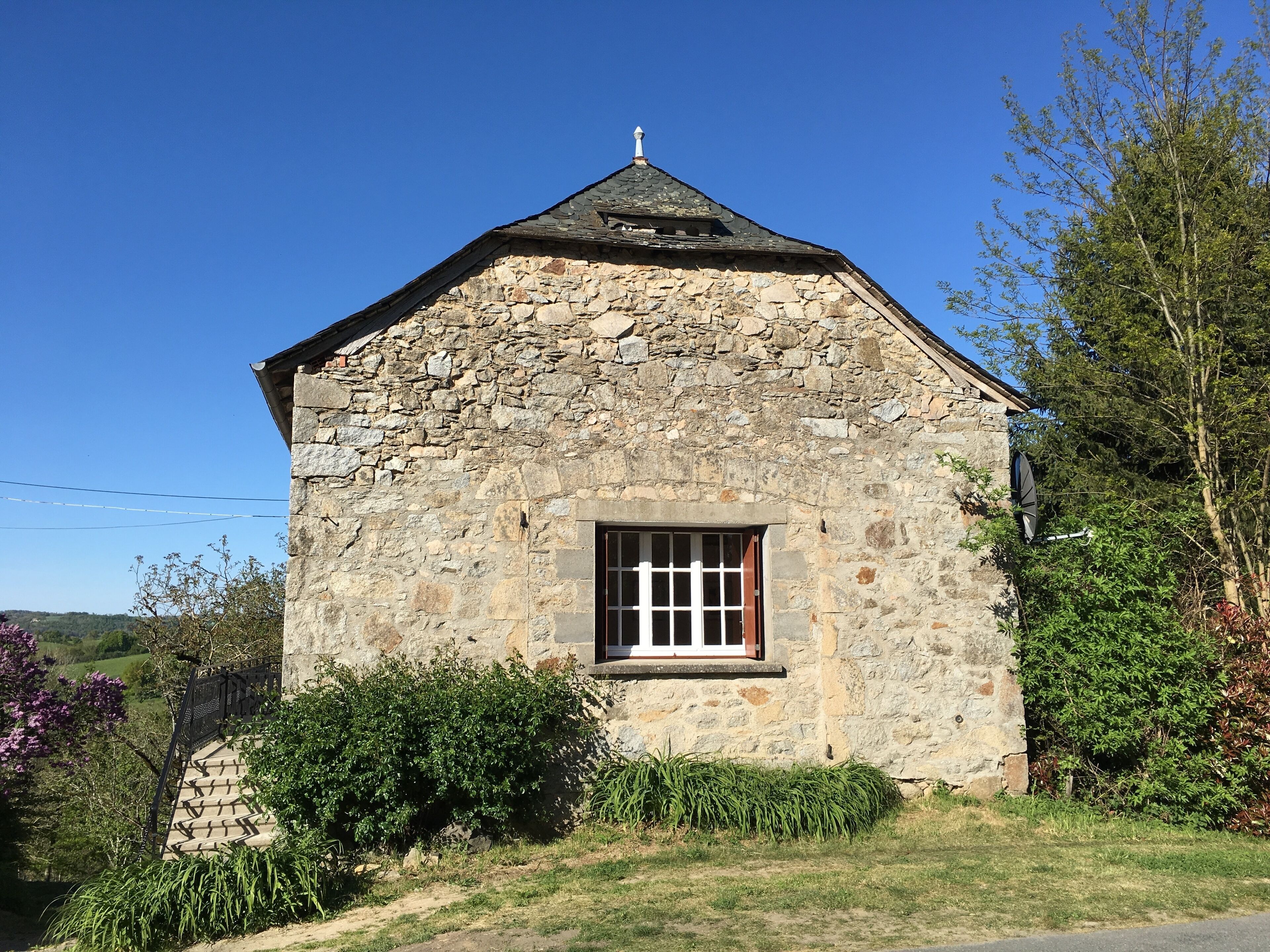A stone building with a gabled roof, a window with white shutters, and a small porch area.