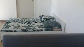 A room with a bed covered in a floral-patterned bedspread, a grey sofa with matching pillows, and a white door. - Uzes (8km), lovely guest house with swimming pool. (Serviers-et-Labaume)