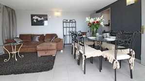 Una sala de estar con un sofá marrón, una mesa de comedor con sillas y una cocina al fondo.