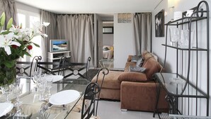 Una sala de estar con una mesa de comedor de vidrio, un sofá marrón y un televisor al fondo.