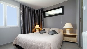 Un dormitorio con cama, dos mesitas de noche con lámparas, una ventana con cortinas y un espejo en la pared.