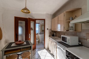 A compact kitchen with a microwave, sink, and a small dining area with a table and chairs. - Pentone - One Bedroom Apartment, Sleeps 4 (Cervione)