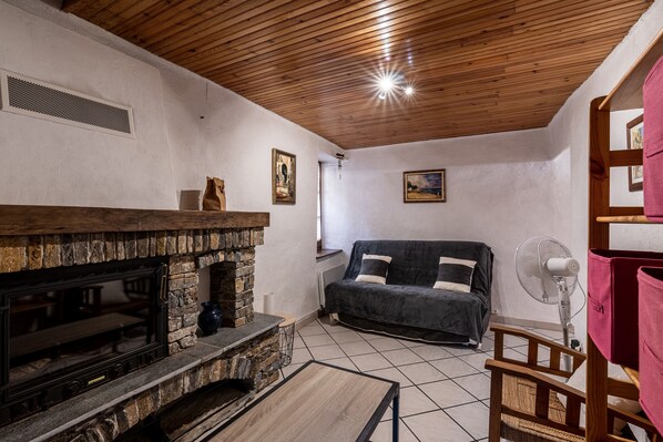 A cozy living room with a stone fireplace, a wooden ceiling, a sofa, and a fan.