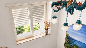 A room with a blue sofa, a small wooden table, a dresser, a window with blinds, and a hanging decoration. - Beb La Bella Annacapri  (Anacapri)