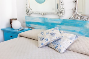 Una cama con ropa de cama color crema y almohadas estampadas con motivos de estrellas azules, un globo blanco sobre una mesita de noche azul, y un espejo con un marco ornamentado.