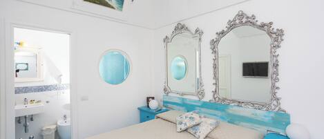 A bedroom with a bed, two mirrors, a dresser, and a bathroom visible through an open door.