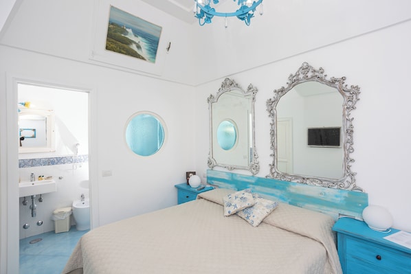 A bedroom with a bed, two mirrors, a dresser, and a bathroom visible through an open door.