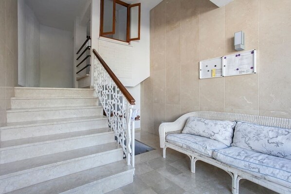 Een trap met witte treden en een houten leuning, leidend naar een kamer met een witte bank en een prikbord aan de muur.