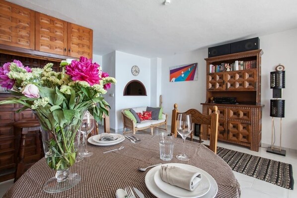 A dining area with a round table set for four, a vase of flowers, and a bookshelf in the background. - Altea Beach Front 'Oden 5' < 4 persons (Altea)