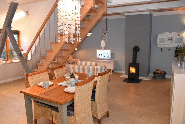 A cozy dining area with a wooden table, wicker chairs, and a hanging light fixture. - Dannauer Reetkate near Weissenhäuser Strand. Bike-friendly, close to the Baltic Sea! (Oldenburg in Holstein)
