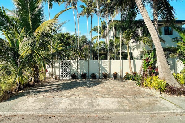 A paved driveway leading to a gated entrance with palm trees and tropical plants. - Art Deco APT w Pool One Mile to Beach Pets Welcome (Lake Worth)