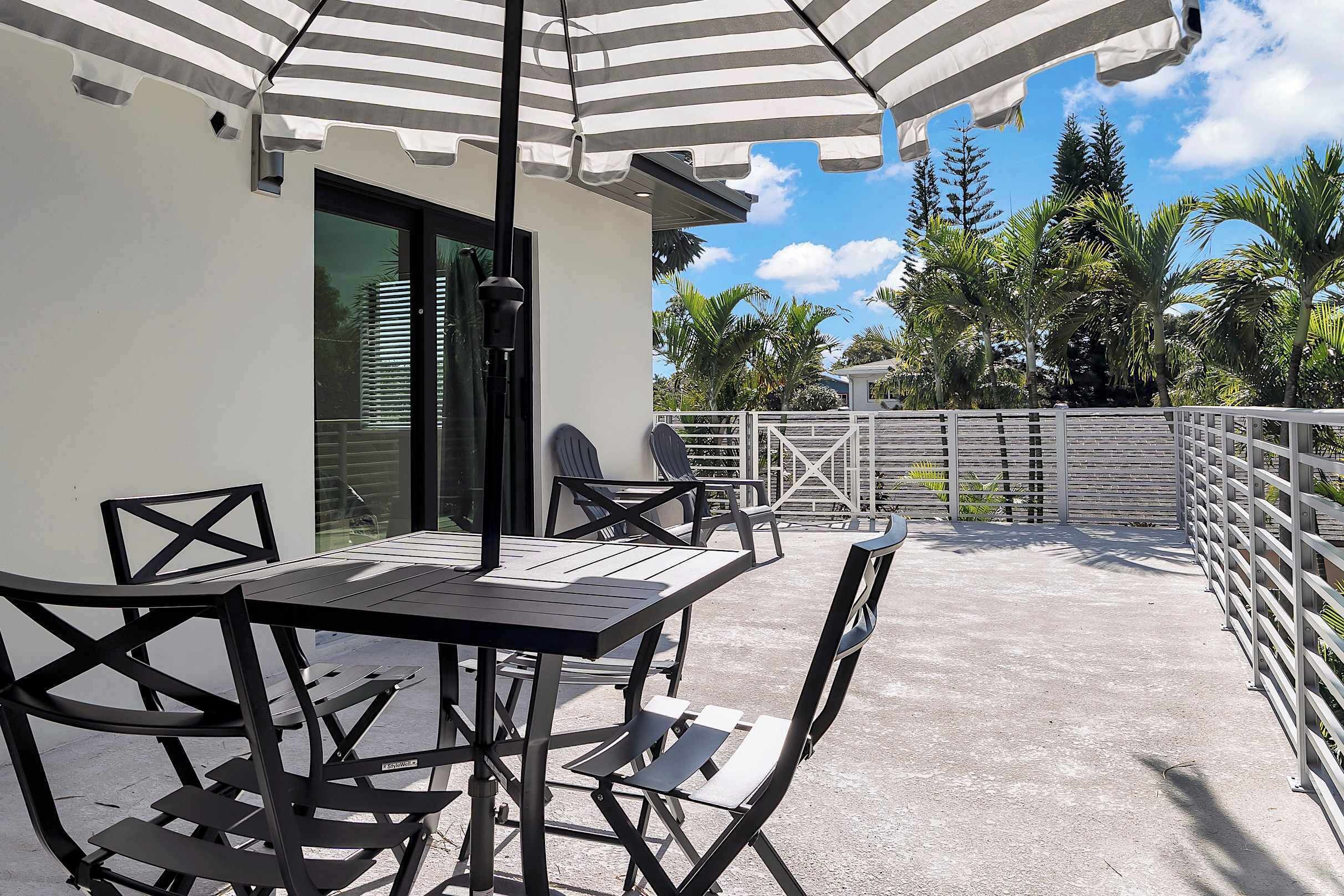 Een terras met een tafel en stoelen, een gestreepte parasol en uitzicht op palmbomen.