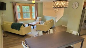 Een gezellige woonkamer met een bank, stoelen, een salontafel en een eettafel.