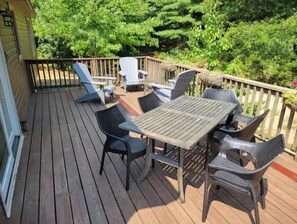 A wooden deck with outdoor furniture including a table and chairs, surrounded by a wooden railing and lush greenery.