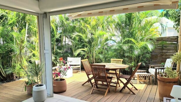 An outdoor patio with a wooden table and chairs, surrounded by lush greenery and potted plants. - JARDIN TROPICAL - 2-bedroom apartment (Le Gosier)