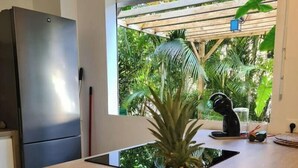 A kitchen with a wooden countertop, a fruit bowl containing a pineapple, bananas, and a lime, a black faucet, and a window with a view of greenery. - JARDIN TROPICAL - 2-bedroom apartment (Le Gosier)