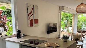 A modern kitchen with a central island, white cabinetry, and a large window providing a view of the outdoors. - JARDIN TROPICAL - 2-bedroom apartment (Le Gosier)