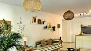 A modern living room with a striped sofa, a woven chair, and a large potted plant. - JARDIN TROPICAL - 2-bedroom apartment (Le Gosier)