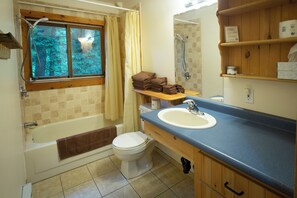 A bathroom with a bathtub, toilet, sink, and a window with a view of trees.
