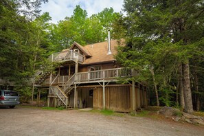 A rustic cabin with a wooden deck and stairs leading to a balcony.