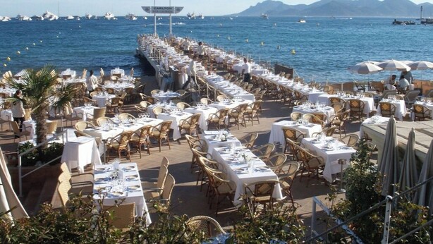 Restaurante frente al mar con terraza y mesas y sillas dispuestas para comer, con vista al océano.