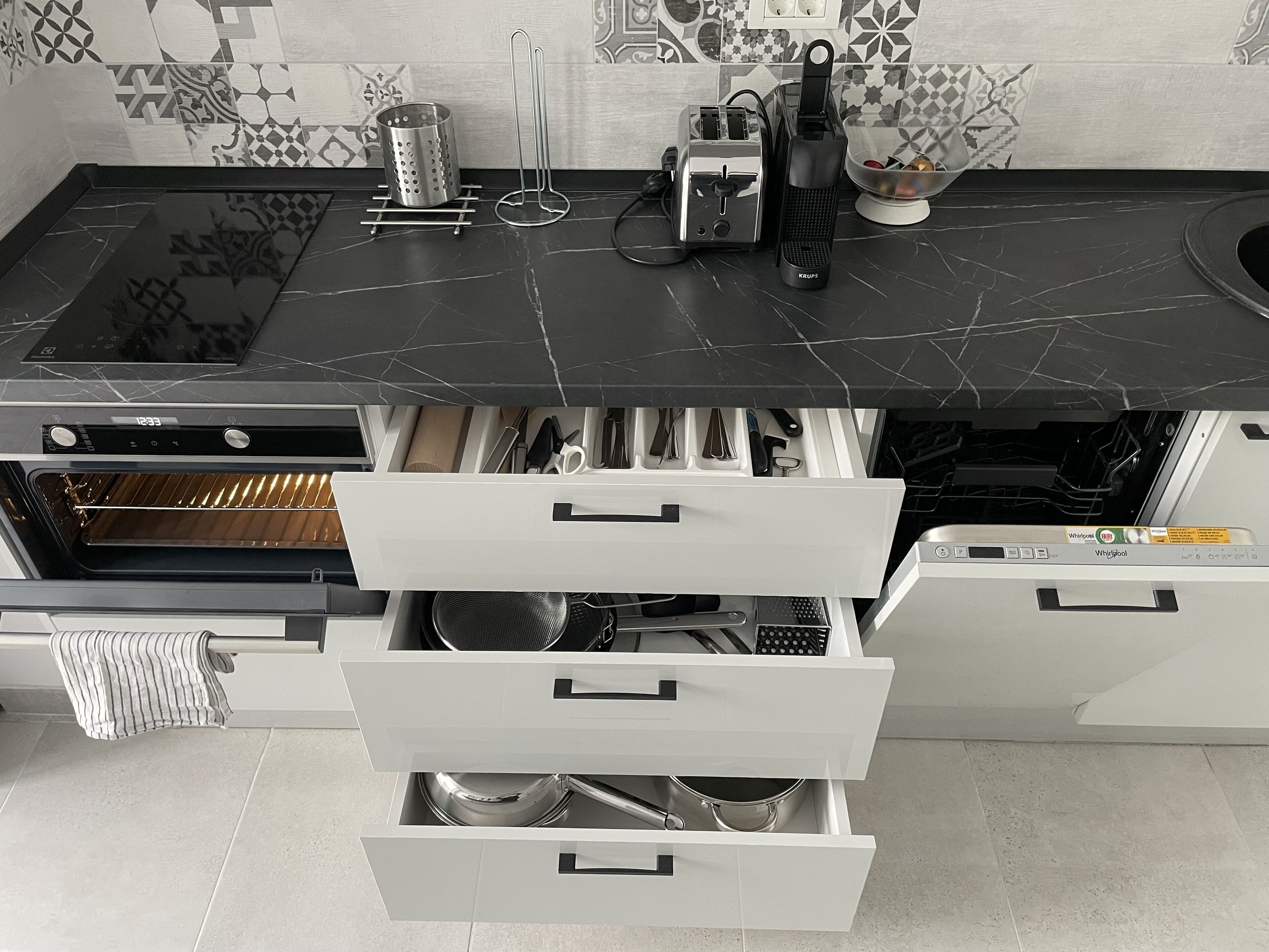 Una cocina moderna con encimera de mármol negro, horno empotrado y armarios blancos con varios cajones.
