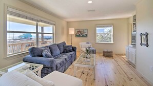 A spacious living room with a grey sofa, a white armchair, a glass coffee table, and a view of the beach through large windows. - Gulf Shores Rental w/ Large Porch - Beach View! (Gulf Shores)