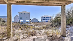 A wooden deck leading to a beach area with houses in the background. - Gulf Shores Rental w/ Large Porch - Beach View! (Gulf Shores)
