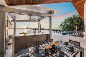 An outdoor dining area with a view of the water and sunset, a covered seating area, and a poolside lounge.