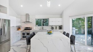 A modern kitchen with a marble island, stainless steel appliances, and large windows. - Bayfront Escape Poolside Luxury Villa with Sunset Views (North Bay Village)