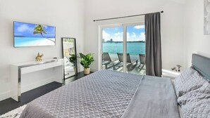 A bedroom with a bed, a desk, a TV, a plant, and a view of the sea. - Bayfront Escape Poolside Luxury Villa with Sunset Views (North Bay Village)