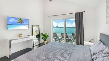 Une chambre avec un lit, un bureau, une télévision, une plante et une vue sur la mer.