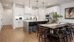A modern kitchen with white cabinets, a central island, bar stools, and a dining table. - Desert Daydream: Desert Color Lagoon + Beaches (St. George)
