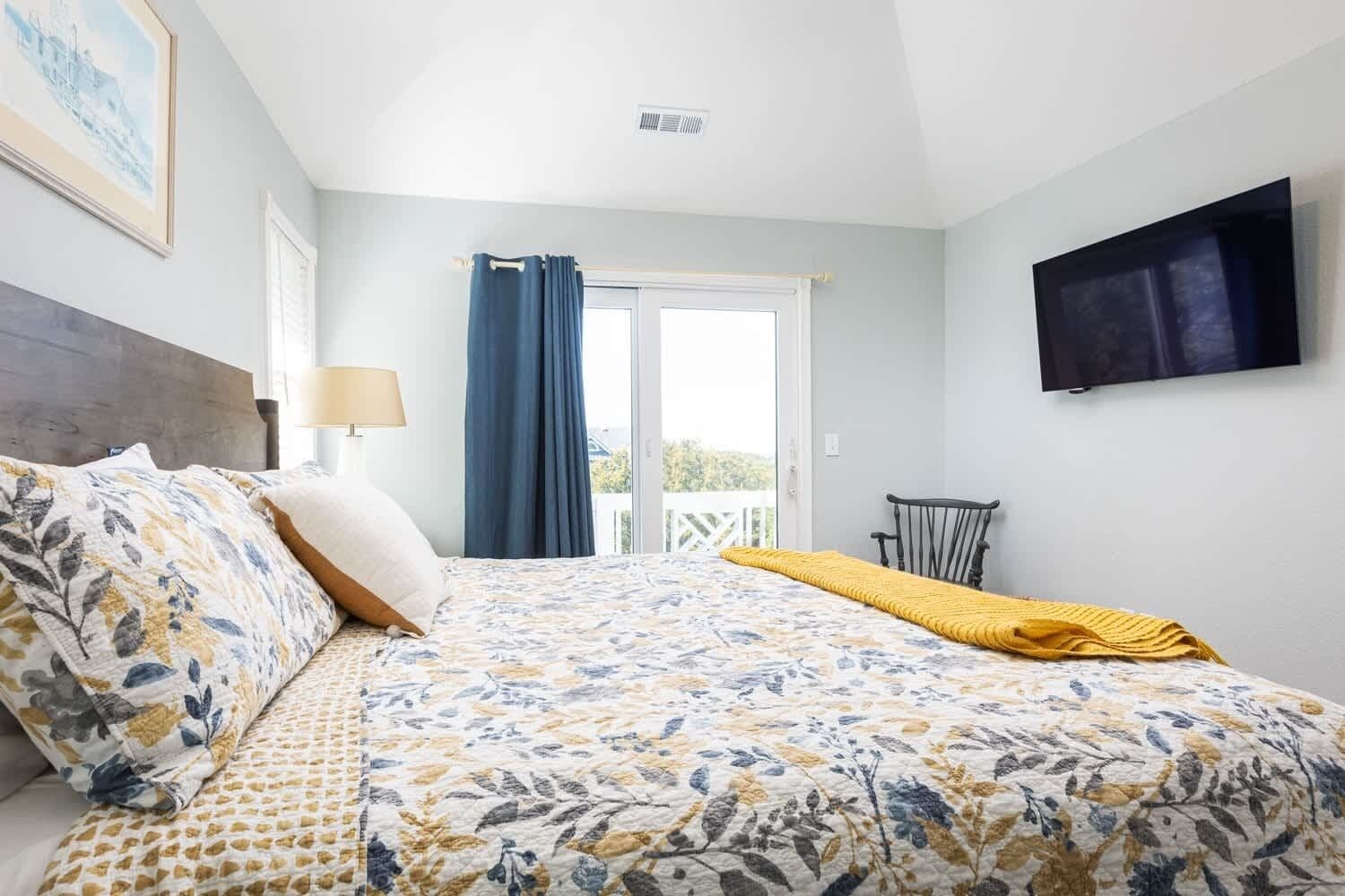 A bedroom with a bed, a chair, a TV, and a window with curtains.