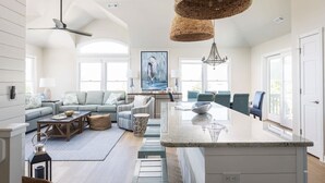 A spacious living area with a large island, a ceiling fan, and a dining area with blue chairs. - 5 Min to Beach, Pool, Hot Tub, Resort Amenities (Corolla)