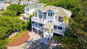 A multi-story coastal house with a balcony, surrounded by lush greenery and a clear view of the ocean. - 5 Min to Beach, Pool, Hot Tub, Resort Amenities (Corolla)