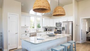 A modern kitchen with white cabinetry, a large island, and blue bar stools. - 5 Min to Beach, Pool, Hot Tub, Resort Amenities (Corolla)