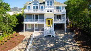 A two-story beachfront property with a prominent yellow door, multiple balconies, and a well-maintained garden. - 5 Min to Beach, Pool, Hot Tub, Resort Amenities (Corolla)