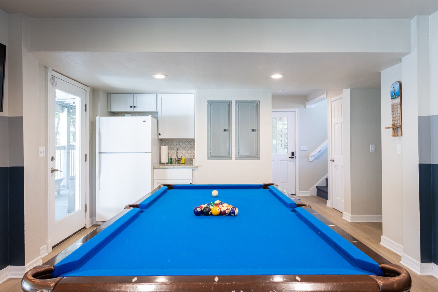 A pool table in a room with white cabinets, a refrigerator, and a door leading to a balcony.